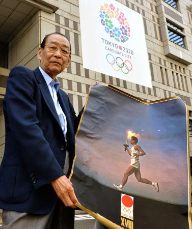　２０２０年東京五輪招致の壁面広告の下で、１９６４年東京五輪当時のポスターを持つ＝１３年８月３０日