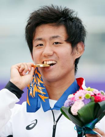 　男子シングルスで優勝し、笑顔で金メダルをかむ西岡良仁＝仁川（共同）