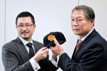 会見でＯＢ会から帽子をプレゼントされる三田学園・羽田監督（右）。左は南ＯＢ会長