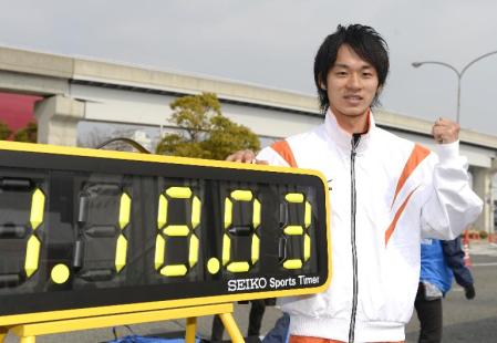 　１時間１８分３秒の日本新記録を示す掲示の横でポーズをとる、男子で初優勝した高橋英輝