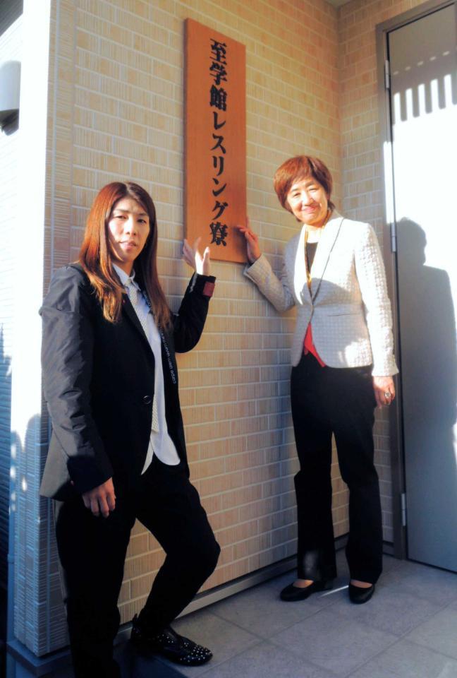 　至学館大レスリング部の寮が完成し、看板に手をかけポーズをとる吉田沙保里（左）と谷岡郁子学長（共同）