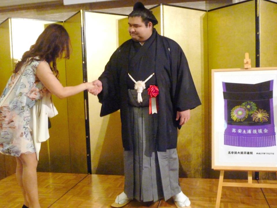 　後援会から贈られた花火の化粧まわしの横でファンと握手する高安（右）