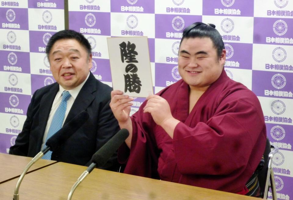新しこ名が書かれた色紙を手に笑顔の隆の勝。左は師匠の千賀ノ浦親方