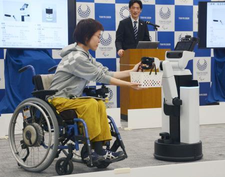 　車いすの女性に飲み物が入ったかごを手渡すロボット＝１５日午前、東京都港区