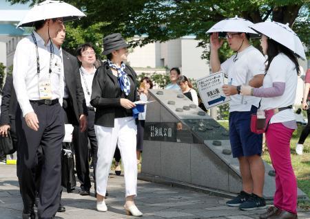　ビーチバレーの五輪テスト大会の会場を訪れ、傘をかぶって活動するボランティア（右の２人）の様子を視察する東京都の小池百合子知事（手前左から２人目）＝２８日午後、東京都品川区
