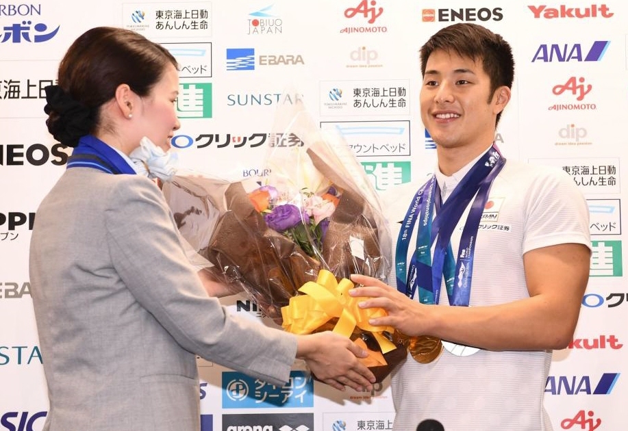 　全日空関係者から祝福の花束を渡される瀬戸大也（右）＝羽田空港（撮影・園田高夫）