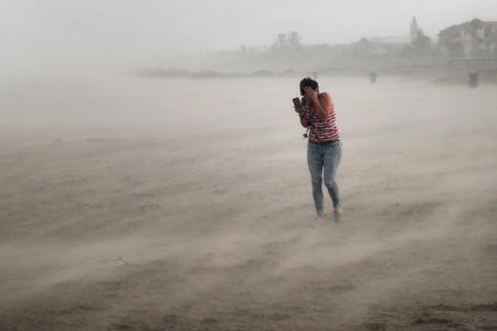 　ハリケーン「ドリアン」により吹き荒れる風や砂の中、ビーチを歩く女性＝２日、米南部フロリダ州（ゲッティ＝共同）