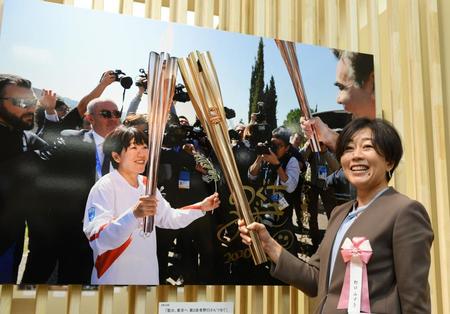 　聖火リレーで実際に使われたトーチを写真に近づけるアテネ五輪女子マラソン金メダリストの野口みずきさん（代表撮影）