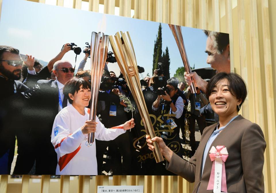 　聖火リレーで実際に使われたトーチを写真に近づけるアテネ五輪女子マラソン金メダリストの野口みずきさん（代表撮影）