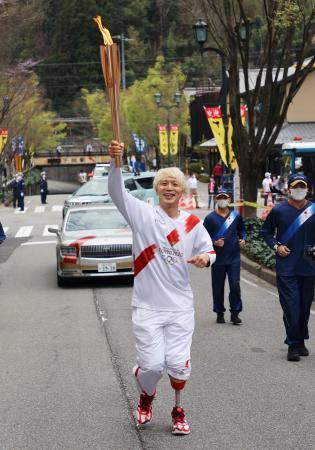 　岐阜県下呂市でトーチを掲げて走る聖火ランナーの大前光市さん＝４日午前（代表撮影）