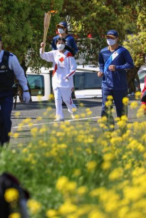 　菜の花が咲く奈良県五條市のコースを、聖火のトーチを掲げて走るランナー＝１１日午前