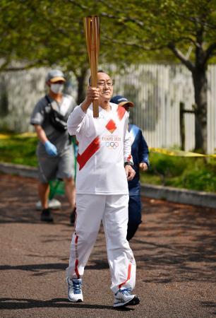 　聖火のトーチを掲げて走る西村成生さん＝１４日午前、大阪府吹田市の万博記念公園