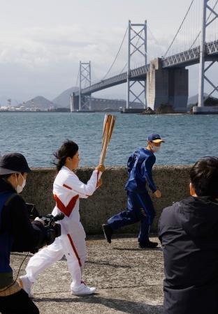 　聖火のトーチを掲げて瀬戸大橋（奥）の近くを走る岩中楓さん＝１８日午前、香川県坂出市の与島