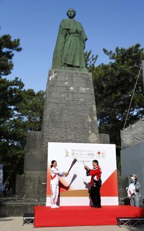 　坂本龍馬像前でトーチを掲げる島崎和歌子さん（左）＝１９日午前、高知市