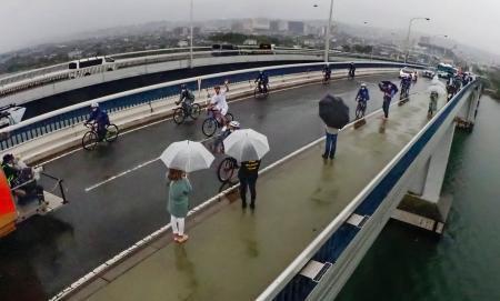 　滋賀県の大津市（奥）と守山市を結ぶ琵琶湖大橋を自転車で走る聖火ランナー＝２７日午前