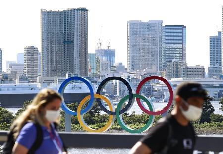 　五輪マークのモニュメントの前を歩くマスク姿の人たち＝７月２１日午後、東京都港区