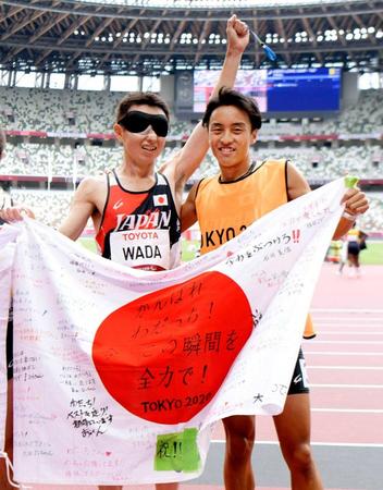 　銀メダルを獲得し、日の丸を掲げる和田伸也。右は伴走者の長谷部匠さん