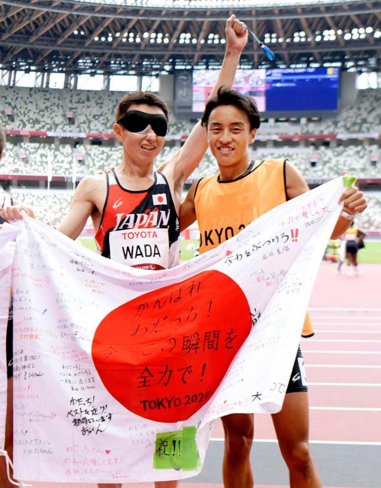 　銀メダルを獲得し、日の丸を掲げる和田伸也。右は伴走者の長谷部匠さん