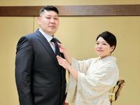 　真美夫人（右）にネクタイを締めてもらう元常幸龍の佐久間貴之氏