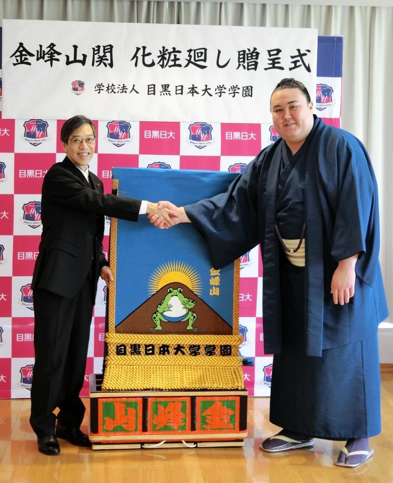 　化粧まわしを贈られ、目黒日本大学学園の小梛治宣理事長（左）と握手する金峰山