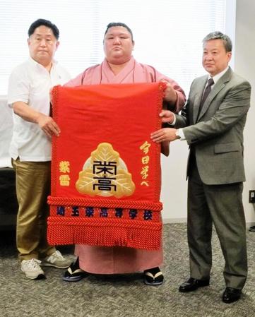 　母校・埼玉栄高から贈呈された化粧まわしを持つ紫雷（中央。左は山田道紀監督、右は町田弦校長）