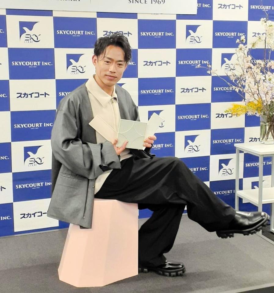 　こだわりのタイルを持ち、プレゼントするスツールに座る高橋大輔さん