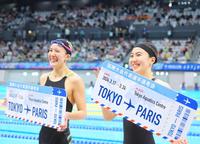 　女子２００メートル個人メドレーでパリ五輪代表に決まり、ボードを手に笑顔の松本信歩。左は大橋悠依＝３月２４日