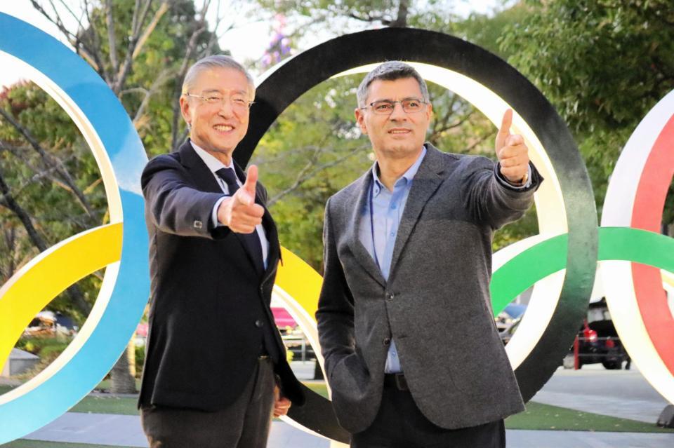 五輪モニュメントの前で射撃のポーズを決めるユスフ・ディケチ（右）と、松丸喜一郎会長