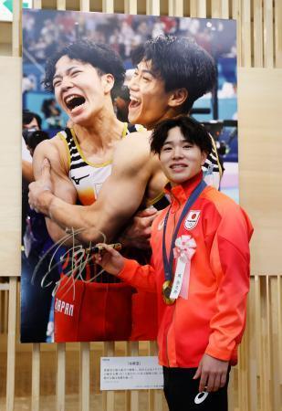 　「２０２４年報道写真展」で、自身の写真にサインする体操男子の岡慎之助選手＝１１日午前、東京都中央区の日本橋三越本店