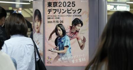 　聴覚障害者の国際スポーツ大会「デフリンピック」のポスターの前を行き交う人たち＝１４日午後、東京都港区