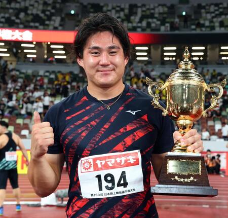 　男子やり投げで優勝し、トロフィーを手に笑顔を見せる崎山雄太