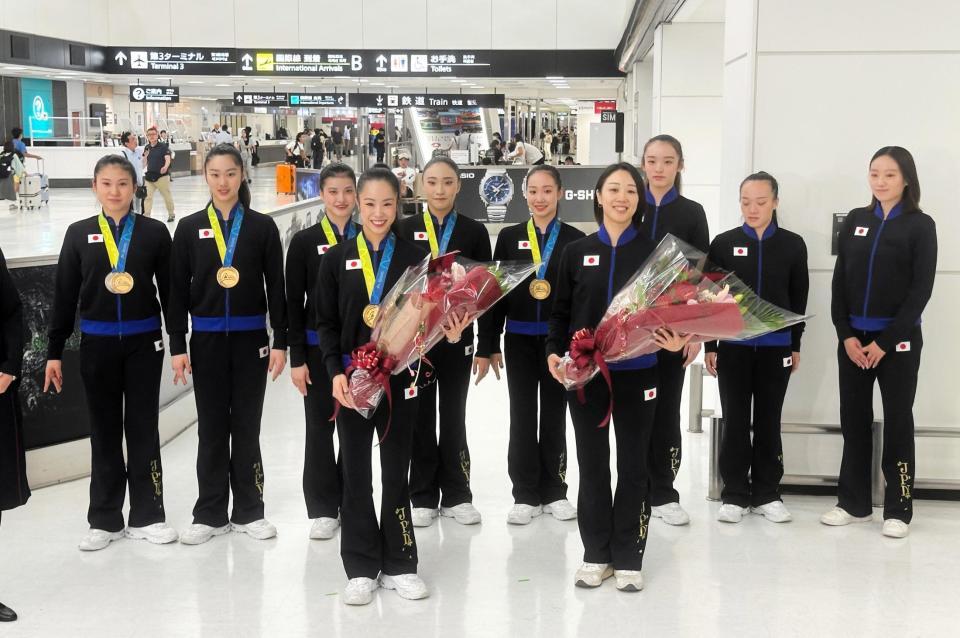 　世界選手権から帰国し、花束を手に笑顔の鈴木歩佳主将（手前左）、村田本部長（同右）ら＝８月２６日