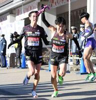 　６区・後村（左）から受け取ったタスキを掲げてスタートする国学院大・高山（撮影・伊藤笙子）