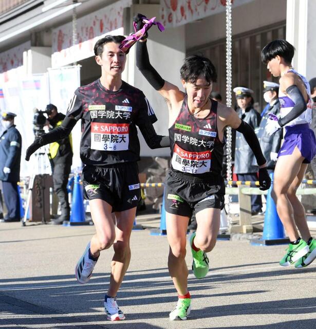 　６区・後村（左）から受け取ったタスキを掲げてスタートする国学院大・高山（撮影・伊藤笙子）