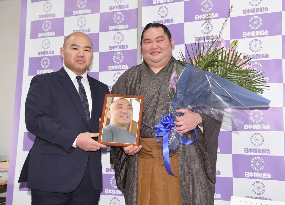 引退会見で志賀ノ浦親方（左）から贈呈された花束と恩師で鹿児島商業高校相撲部元監督の禧久昭広さんの遺影を手に笑顔を見せる大奄美（撮影・開出牧）