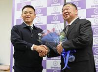 定年前の記者会見で、湊川親方（左）から花束を受け取り握手する常盤山親方