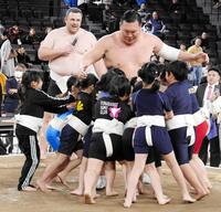 元大関把瑠都のカイド・ホーヴェルソンさんがマイクを持つ前で、女の子と相撲を取る白鵬翔さん