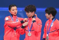 表彰台で佐藤駿㊥のメダルを整える坂本花織。右は鍵山優真