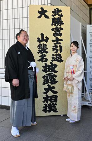 看板の前で記念撮影する大山親方（元北勝富士）（左）と真美夫人