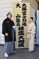 看板の前で記念撮影する大山親方（元北勝富士）（左）と真美夫人