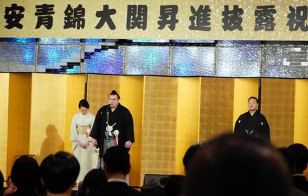 安治川親方（右）とおかみさんを背に、メモを持たず開宴のあいさつを行う安青錦＝都内
