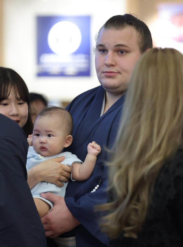 帰国した空港で赤ちゃんを抱く安青錦（撮影・西岡正）