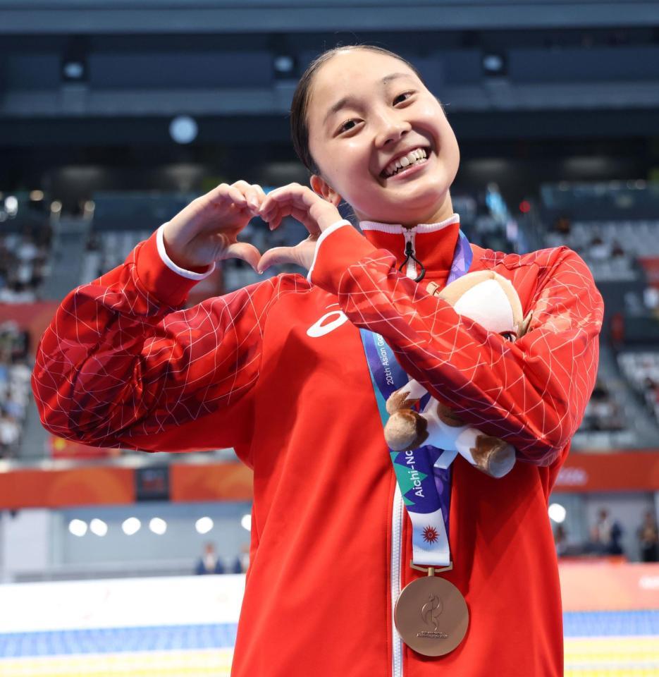 女子４００ｍ個人メドレーの表彰式を終え、カメラマンに向けてハートマークを作る成田実生（撮影・伊藤笙子）