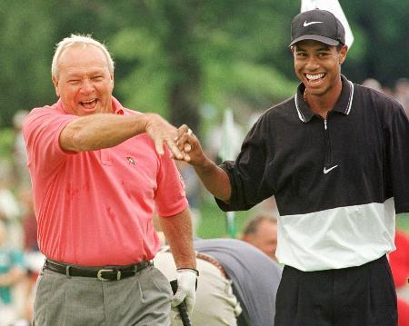 　１９９７年８月、ゴルフのチャリティーマッチでペアを組み笑顔で握手するアーノルド・パーマー氏（左）とタイガー・ウッズ氏。胸に傘のマークのシャツを着用している（ロイター＝共同）
