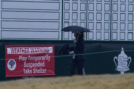 　悪天候によるプレーの一時中断を示した横断幕の前を、傘を差して通る大会関係者＝１３日、米ヒューストン（ＡＰ＝共同）