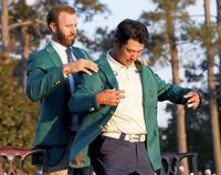 米ゴルフのマスターズ・トーナメントで、日本男子初のメジャー制覇を果たし、グリーンジャケットに袖を通す松山英樹。左は前年優勝のダスティン・ジョンソン＝11日、米ジョージア州のオーガスタ・ナショナルＧＣ（ロイター＝共同）
