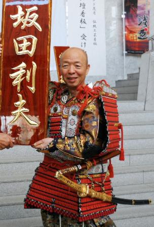 「広島仏壇」による看板を前に笑顔の坂田利夫（右）＝広島県廿日市市