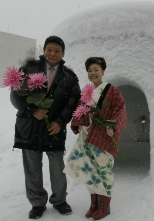 　ダリアの新種「夢の花」を手に、かまくらの前ではしゃぐ中村美律子（右）と増位山＝秋田県横手市