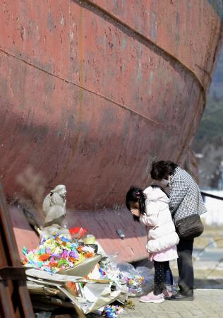 　宮城県南三陸町志津川の防災対策庁舎（中央）。津波で被災した町に電柱が林立する。奥のプレハブは仮設の商店街＝共同通信社ヘリから　（下）陸地に打ち上げられた大型漁船の祭壇で手を合わせる人たち＝宮城県気仙沼市