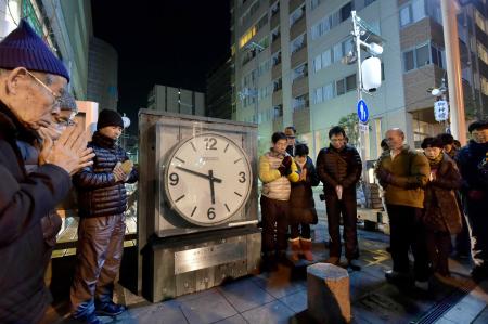 　止まったままの大時計を囲み、発生時刻に黙とうする人たち＝１７日午前５時４６分、兵庫県西宮市